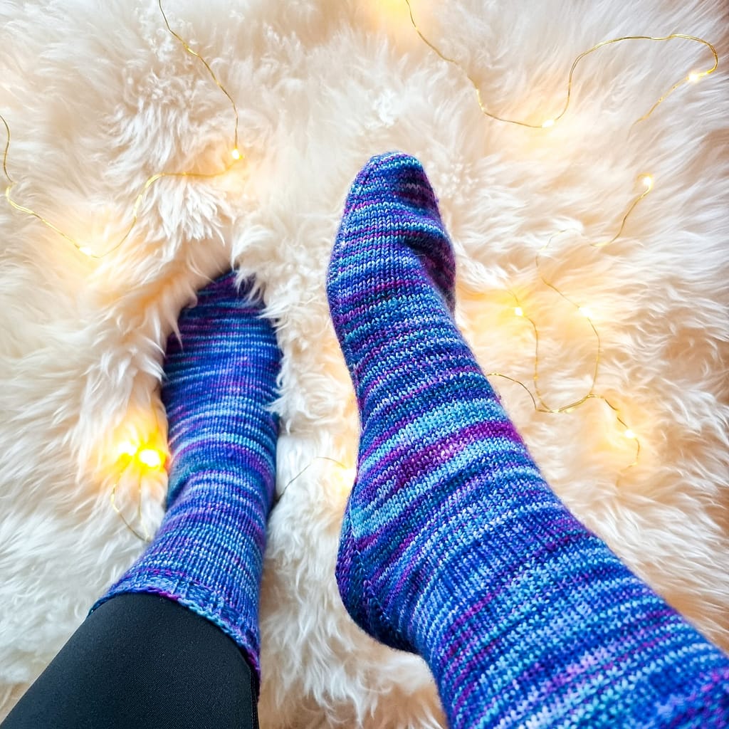A shot of a pair of feet wearing a pair of blue and purple hand-knit socks