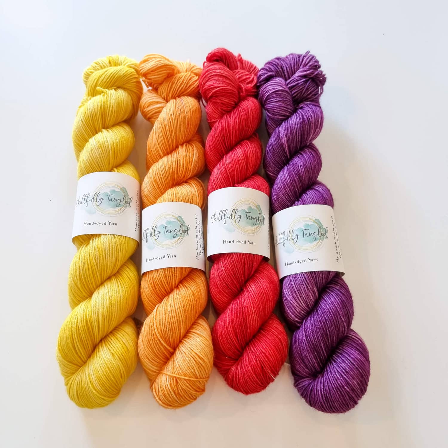 Four skeins of hand dyed merino yarn in yellow, orange, red, and purple. They are a kit for the Geogradient MKAL