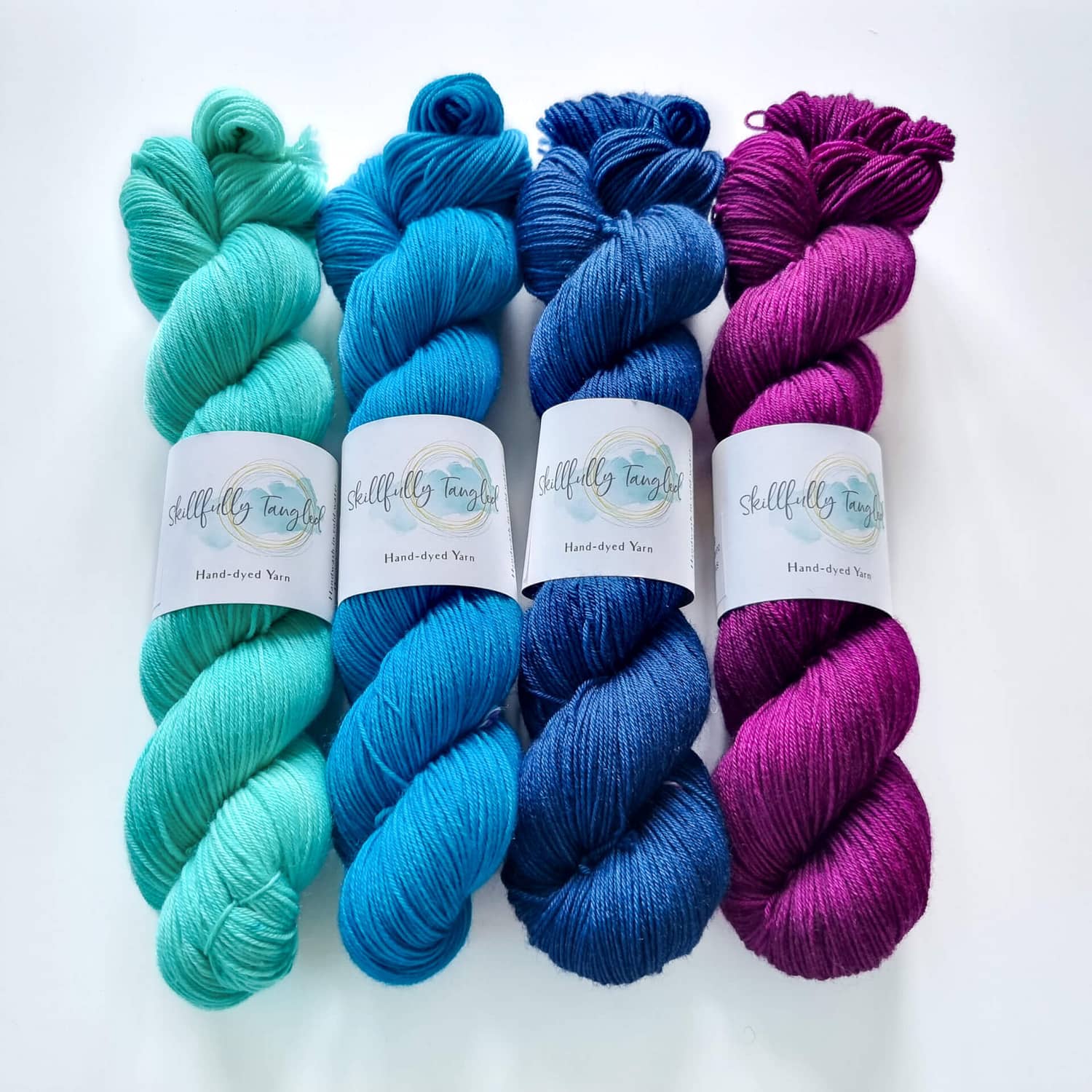 Four skeins of hand dyed merino yarn in light blue, turquoise, indigo and purple. They are a kit for the Geogradient MKAL