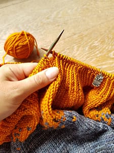 Hand holding knitting needles and ribbing of a sweater