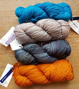 4 skeins of yarn in blue, light grey, grey, and yellow-orange