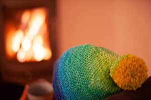 Person wearing a knit hat sitting in front of a fire, photographed from behind