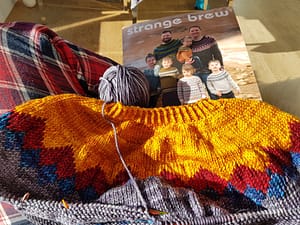 Sweater being knit with a knitting book in the background