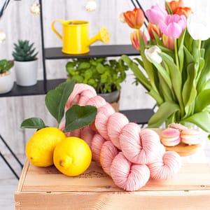 Drei pastellrosa Garnstränge mit einigen Zitronen und Blumen