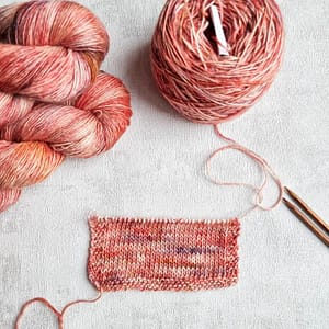A yarn swatch, a cake of yarn and two yarn hanks all in light pink