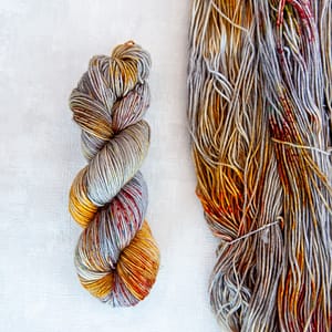 One skein of hand dyed grey yarn with brown, orange, and red speckles