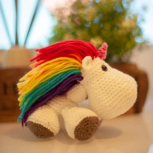 A crochet amigurumi unicorn with rainbow hair