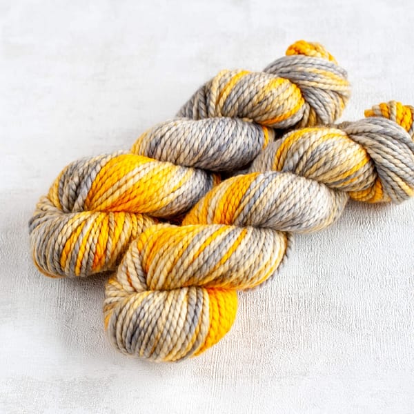 two skeins of grey and yellow yarn in chunky weight laying next to each other