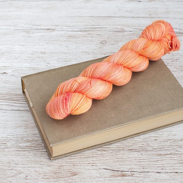 A skein of yarn in the color Peach Sorbet on top of a book