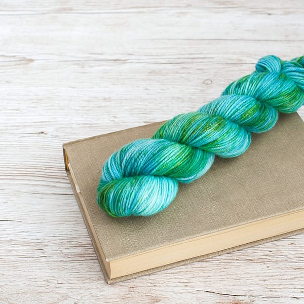 A skein of yarn in the color Pond on top of a book