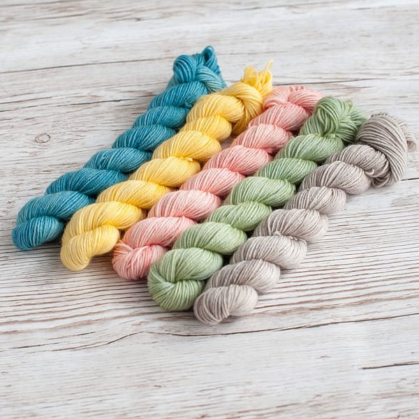 Five mini skeins of yarn in pastel blue, yellow, pink, green, and grey
