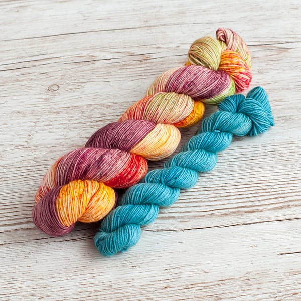 A yarn sock set in the colors Flower Power and Feel the Breeze laying on top of a book