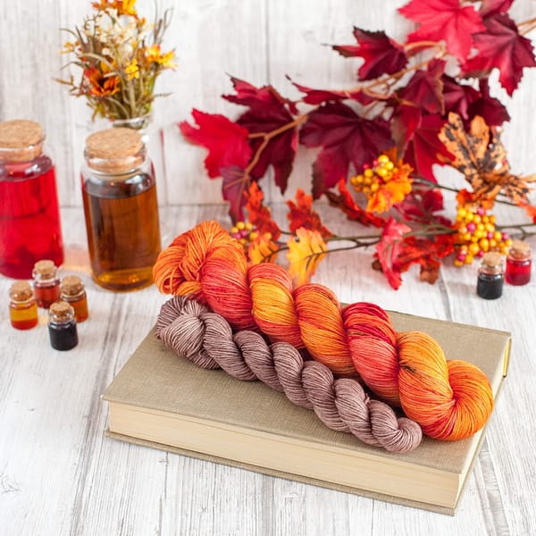A red and orange skein of yarn and a smaller skein of light brown yarn laying next to each other