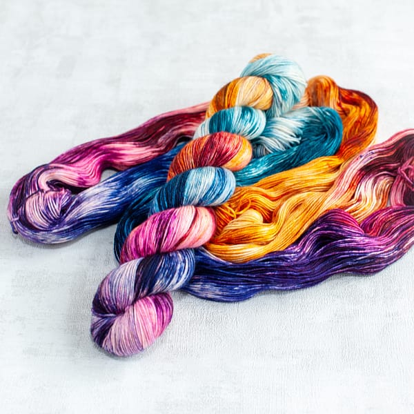 one skein of fingering weight multi-colored yarn laying on top of an open skein in the same colors
