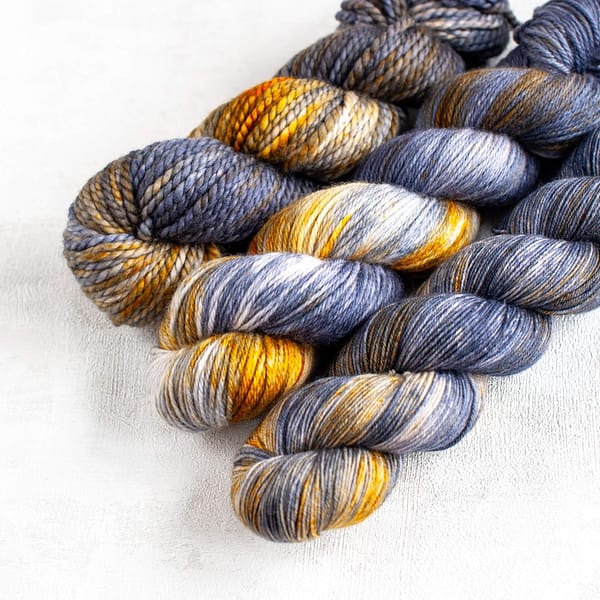 three skeins of dark grey yarn with white spots and yellow speckles