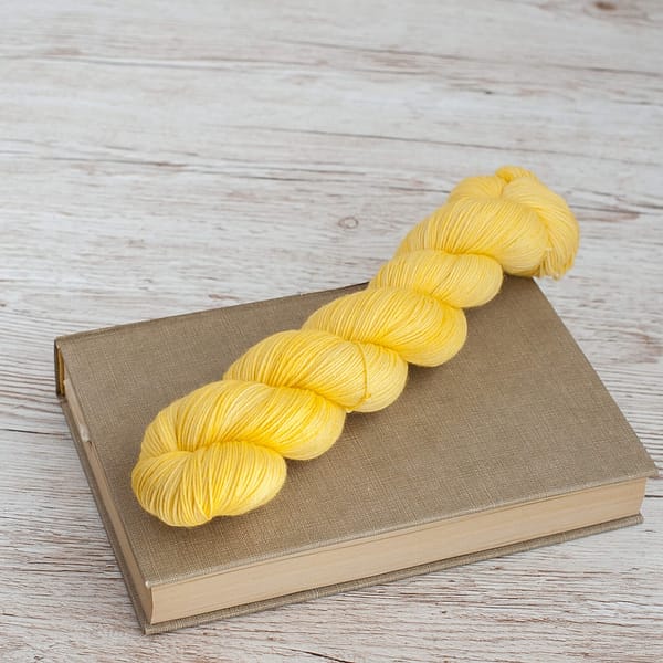 A pastel yellow skein of yarn on top of a book