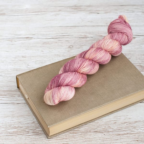 A skein of pink and cream yarn laying on top of a book