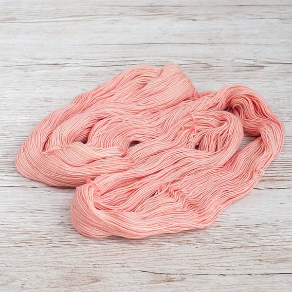 A pastel pink skein of yarn unwound and laid flat