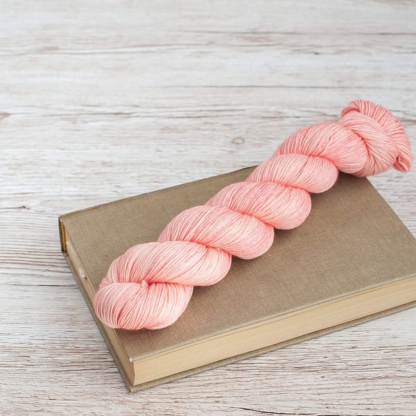 A pastel pink skein of yarn laying on top of a book