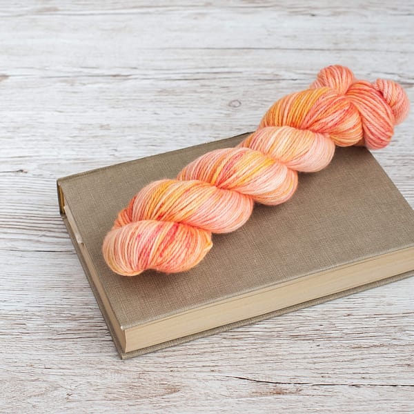 A skein of yarn in the color Peach Sorbet on top of a book