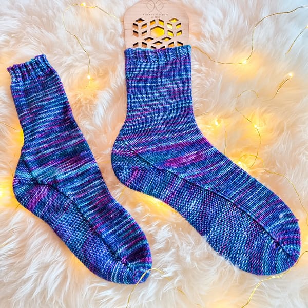 Two blue and purple hand-knit socks laying flat