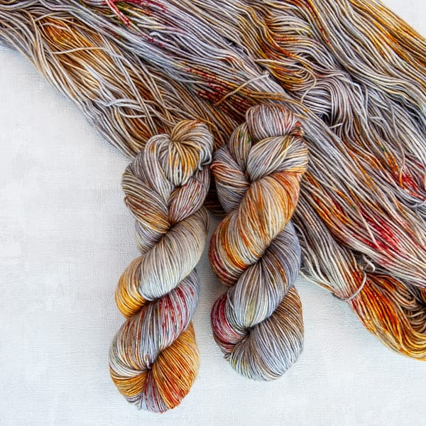 Two skeins of hand dyed grey yarn with brown, orange, and red speckles