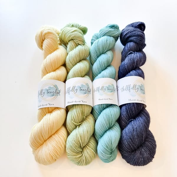 Four skeins of hand dyed merino yarn in yellow, light green, light blue, and denim blue. They are a kit for the Geogradient MKAL