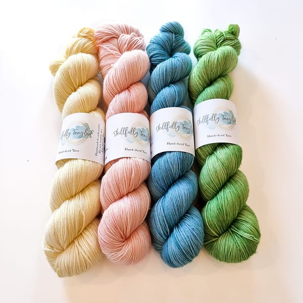 Four skeins of hand dyed merino yarn in pastel colors: yellow, pink, light blue, and green. They are a kit for the Geogradient MKAL