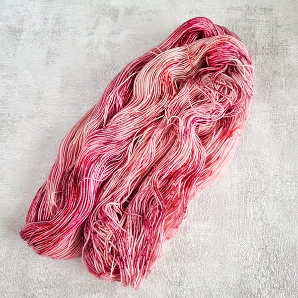 A speckled pink hank of yarn lying open on a white background