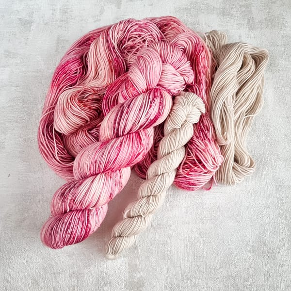 A pink speckled skein of yarn with a smaller grey skein of yarn next to it