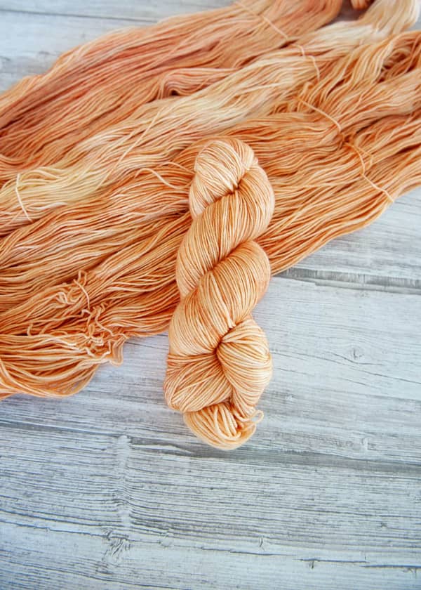 One hanked skein of yarn in the colorway Rosé laying on top of another opened skein of Rosé