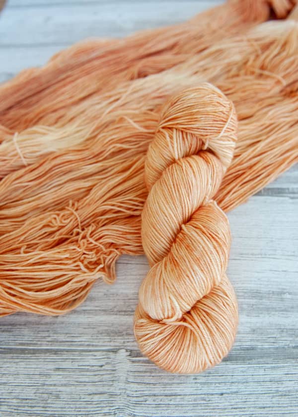 One hanked skein of yarn in the colorway Rosé laying on top of another opened skein of Rosé