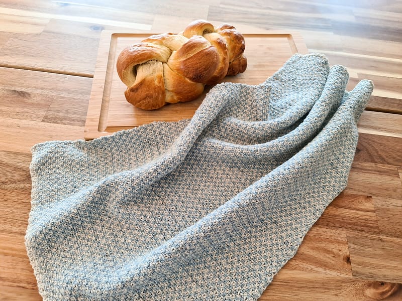 Cottage tea towel laying next to a wooden cutting board with bread on it