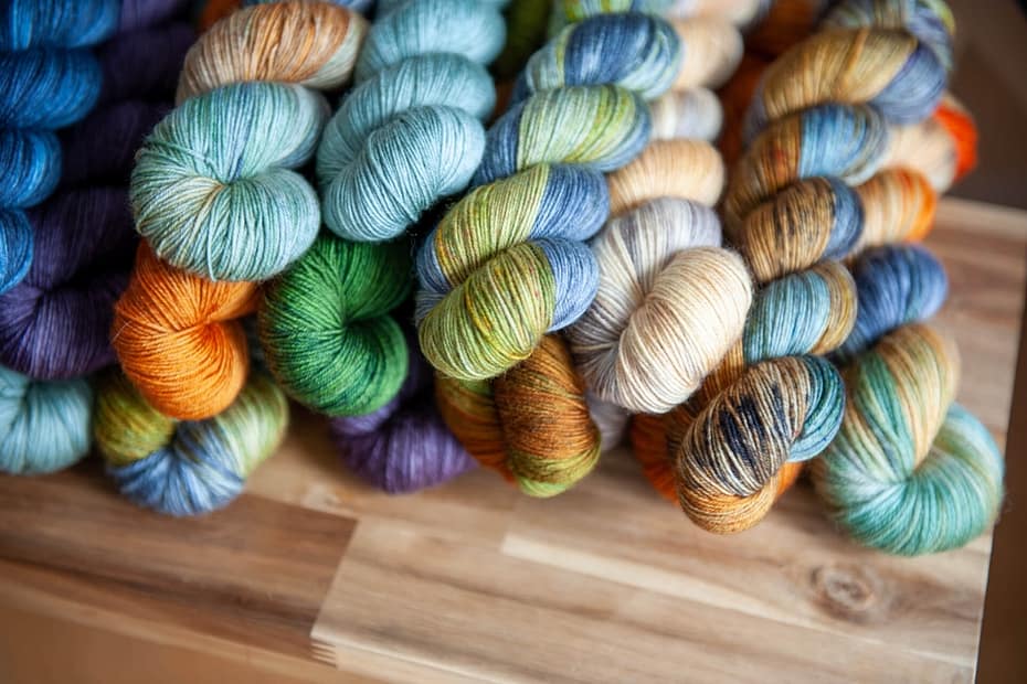 Multiple skeins of yarns laying on top of a wooden bench