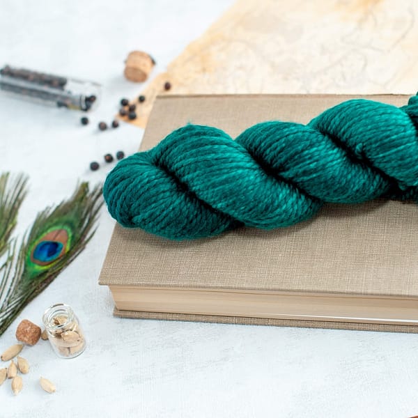 one skein of chunky weight teal green yarn laying on top of a book