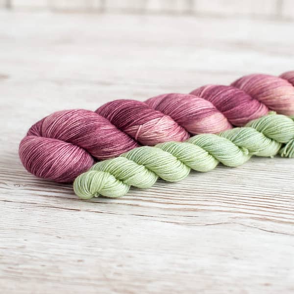 A yarn sock set in the colors Vintage Rose and Cut the Grass laying on top of a book