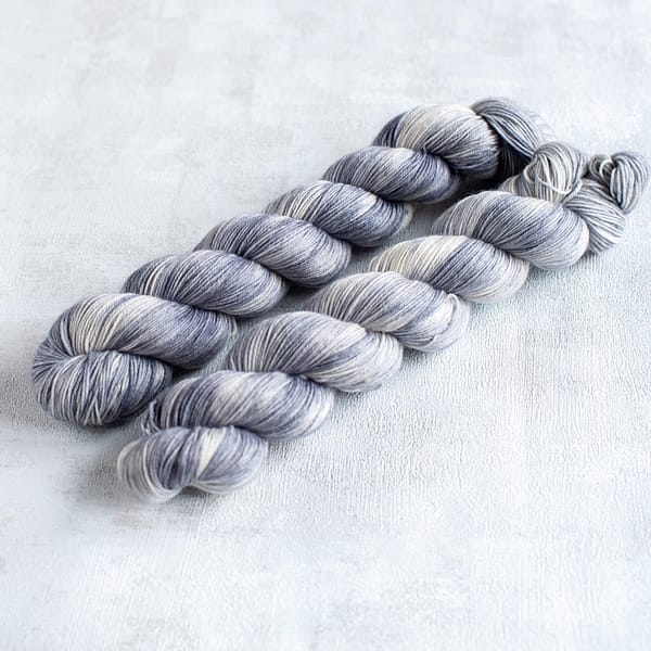 two skeins of fingering weight light grey and white yarn