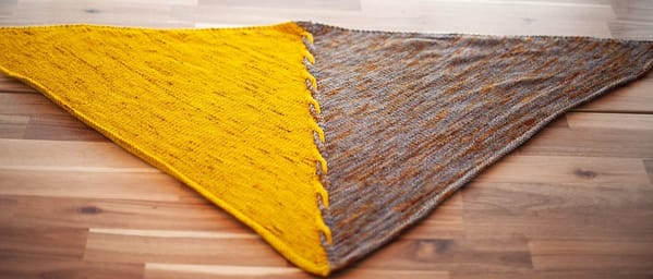 Edge of Winter shawl laid flat, left half of the triangular shawl is yellow, right half is grey