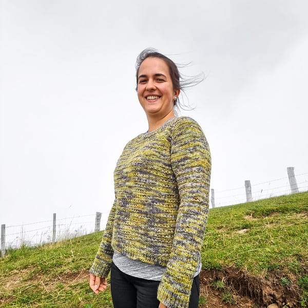 woman wearing a green and grey sweater standing in a green pasture with foggy grey sky