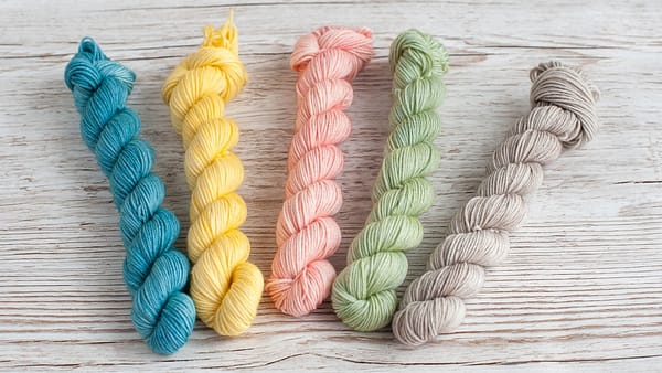 Five mini skeins of yarn in pastel blue, yellow, pink, green, and grey