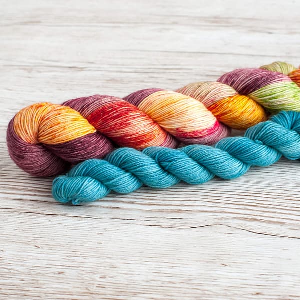 A yarn sock set in the colors Flower Power and Feel the Breez laying on top of a book