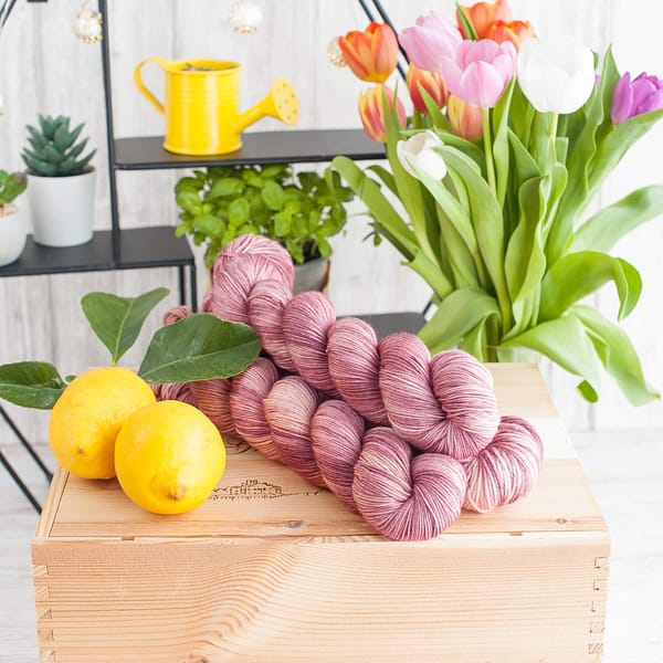 Three skeins of Vintage Rose yarn with lemons and flowers in the background