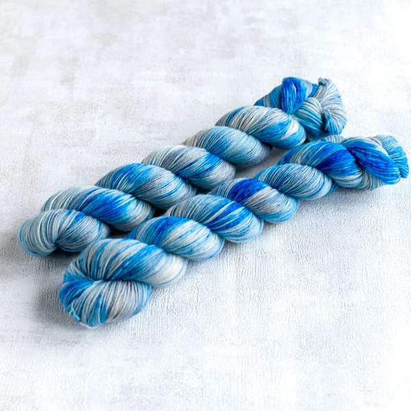 two skeins of fingering weight silver yarn with blue speckles