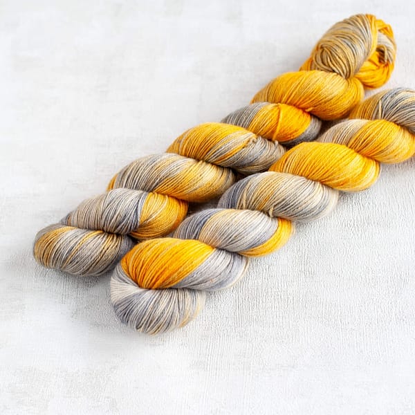 two skeins of grey and yellow yarn in fingering weight laying next to each other