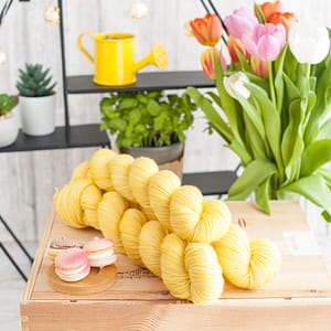 Three skeins of pastel yellow yarn with macarons in the background