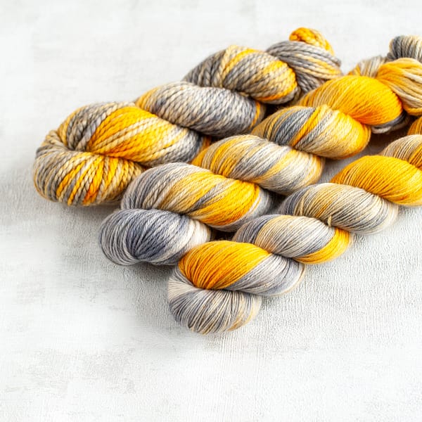 three skeins of grey and yellow yarn laying next to each other
