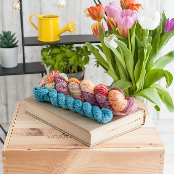 A yarn sock set in the colors Flower Power and Feel the Breez laying on top of a book