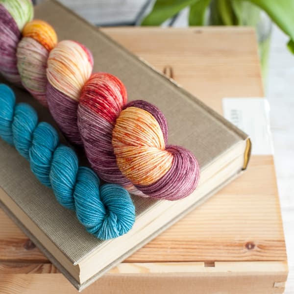 A yarn sock set in the colors Flower Power and Feel the Breeze laying on top of a book