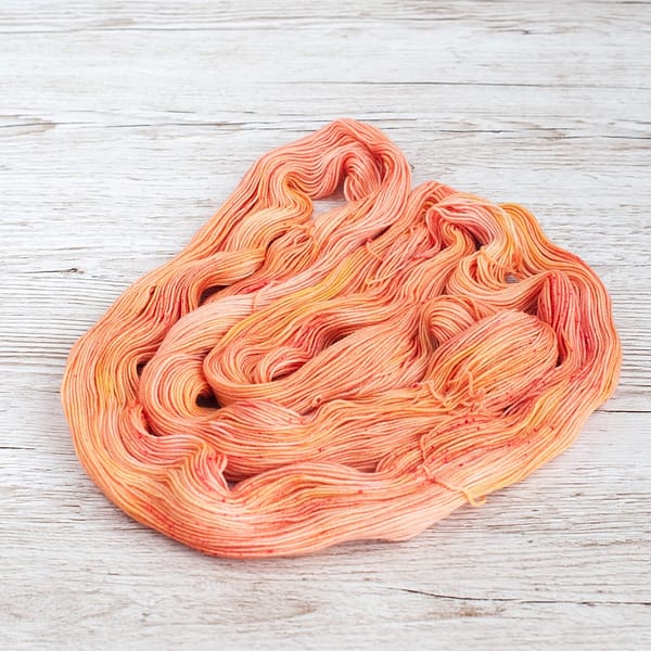 A skein of yarn in the color Peach Sorbet unwound and laid flat