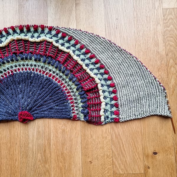 A partially knit Shawlography shawl on the floor